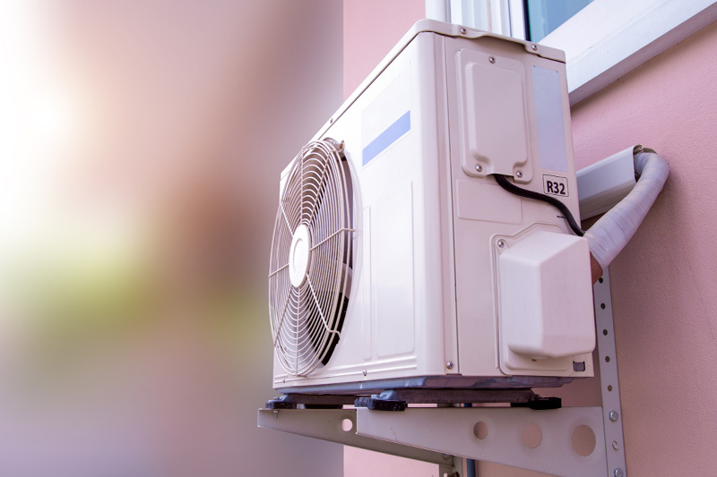 Außenunit einer Klimaanlage an einer Wand mit sichtbarem Lüfter und R32-Kältemittelschlauch.