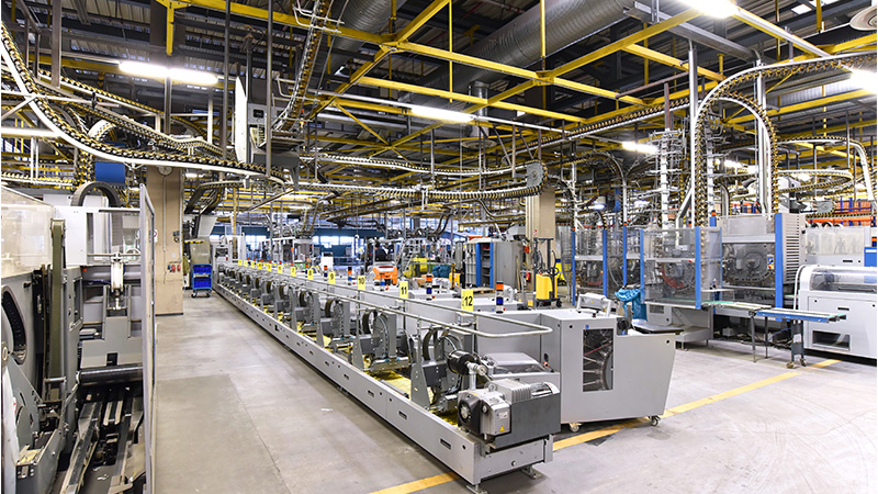 Moderne Industriehalle mit automatisierten Produktionsanlagen, Förderbändern und komplexer Verkabelung an der Decke.